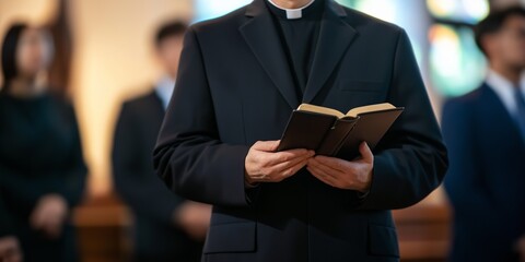 A man in a black suit is reading a book. He is wearing a black robe and is holding a book in his hands. The man is standing in front of a group of people