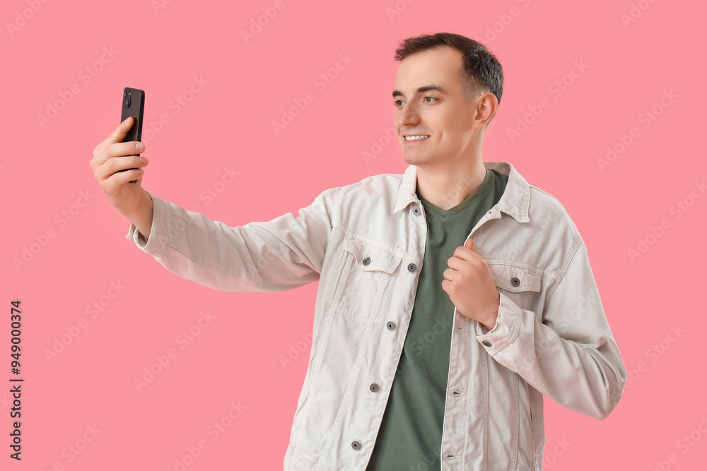 Young man with mobile phone taking video call on pink background