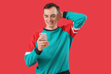 Wall Mural - Young man with mobile phone messaging on red background