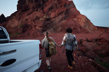 Rear view of young affectionate couple in activewear holding by hands while moving upwards to the direction of mountain