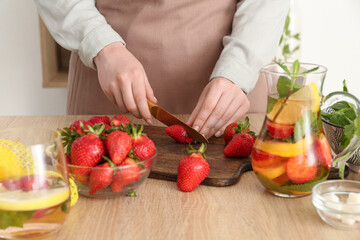 Wall Mural - Woman cutting strawberry for lemonade in kitchen