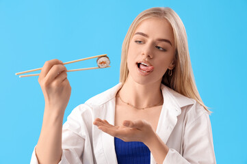 Wall Mural - Young woman with tasty sushi roll on blue background