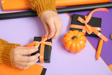 Wall Mural - Woman tying bows on gift boxes for Halloween against purple background