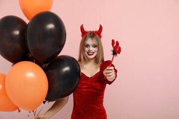 Wall Mural - Young woman dressed for Halloween as devil with balloons on pink background