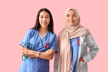 Asian and Muslim female doctors with red ribbons on pink background. World AIDS Day concept