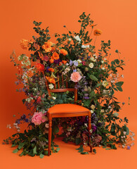 Wall Mural - A bold orange background features a dynamic arrangement of flowers, greenery, and leaves around the chair, adding vibrant color to the studio space.




