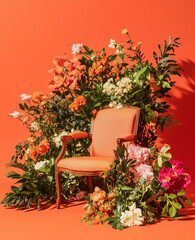 Wall Mural - A bold orange background features a dynamic arrangement of flowers, greenery, and leaves around the chair, adding vibrant color to the studio space.




