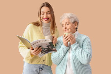 Poster - Young woman and her grandmother with cups of tea reading magazine on beige background