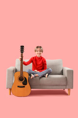 Canvas Print - Cute little boy with guitar sitting on sofa against pink background