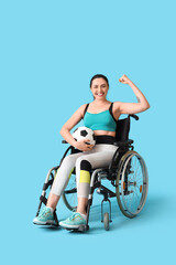 Poster - Sporty young woman in wheelchair with soccer ball showing muscles on blue background