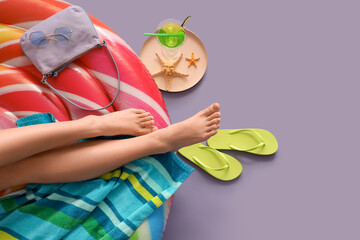 Wall Mural - Young woman sitting on inflatable mattress near flip-flops and cocktail against purple background