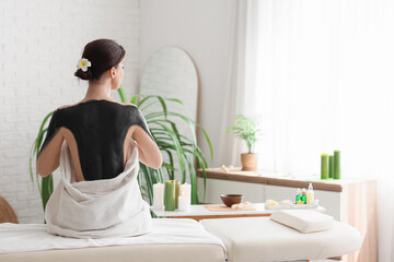 Wall Mural - Young woman with mud sitting in spa salon, back view