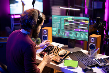Leinwandbilder - Audio engineer following online tutorial on smartphone greenscreen display, learning to use mixing console and add sound effects on songs. Producer creating soundtracks on daw software.