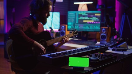 Poster - Songwriter playing acoustic guitar in home studio with greenscreen display running on smartphone app. Musician practices singing on musical instrument with strings, isolated screen. Camera B.