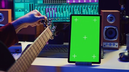 Leinwandbilder - Audio engineer practices tuning his acoustic guitar in home studio, watching a video tutorial online via tablet with greenscreen. Musician learning to play instrument and create music. Camera A.