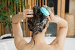 © Pixel-Shot - Beautiful young woman washing hair with shampoo and scalp massager in bathroom at home, back view