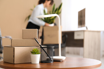 Canvas Print - Moving boxes with plant, lamp and pen cup on desk in office, closeup