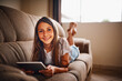 © StarDweller/peopleimages.com - Elearning, portrait and tablet with girl child on sofa in living room of home for development, education or study. Reading, smile and technology with happy student in apartment for remote schooling