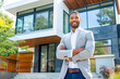 © MVProductions - Confident African American man real estate agent stands proudly outside a modern home, radiating expertise and approachability, ready to assist potential house buyers