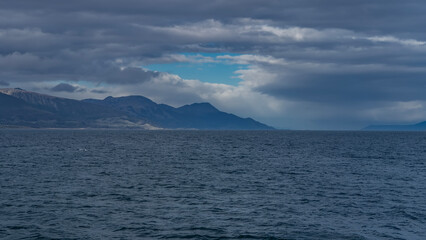 Beautiful seascape. Ripples on the surface of the blue ocean. A mountain range against the background of the sky and clouds in the distance. Argentina, Tierra del Fuego archipelago. The Beagle Channel