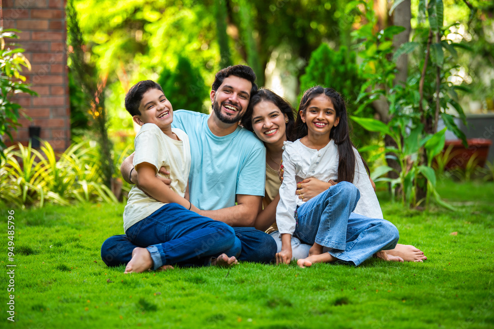 Happy Indian family of four sitting in park, embracing and smiling at ...