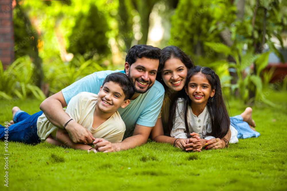 Happy Indian family of four sitting in park, embracing and smiling at ...