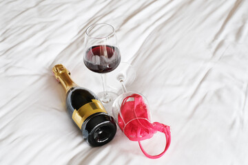 Romantic sex date, red lace panties and wine glasses on the bed. Concept of night of passion, female lingerie. Woman accessories.