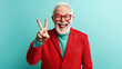 © Keitma - Happy mature man wearing a red jacket isolated on a pastel blue background, studio shot of a old retired male celebrating success and win doing a victory V sign gesture with two fingers from hand