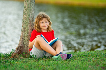 Aufkleber - Cute kid reading book on meadow outdoors. School and education. Nature and park. Early learning. Little boy reading a book in summer park. Concept of childrens recreation without gadgets.