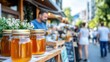© Lens Legacy - A row of honey jars placed on a wooden counter at a street market amid a lively atmosphere with people walking by and surrounded by greenery and flowers.