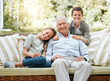 © KayJoint/peopleimages.com - Grandfather, kids and smile in patio on sofa at home for bonding, support and care in England. People, family and outside with happy on portrait on visit as babysitter for break, relax and rest