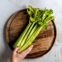 Poster - Fresh celery stalks on a wooden plate with a hand reaching for one.