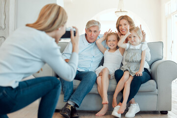 Poster - Grandparents, girls and peace sign with photographer on sofa at home for bonding, support and care. People, family and smile or happy with kids on couch in living room to relax or chill for memories