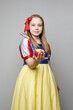 © millaf - Smiling little child girl theater actress in SnowWhite costume holding red apple and standing on white background