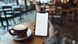 © KYR - Woman's hand holding a smartphone with a white screen, a cup of coffee beside it on a trendy table in a stylish cafe