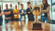 © Lull - Golden trophy award. Gold trophy on a table in front of blurred team members, symbolizing achievement, success, and teamwork.