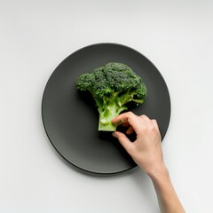 Wall Mural - Hand picking up fresh broccoli on a black plate.