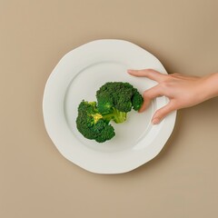 Poster - Hand reaches for a single broccoli floret on a white plate.