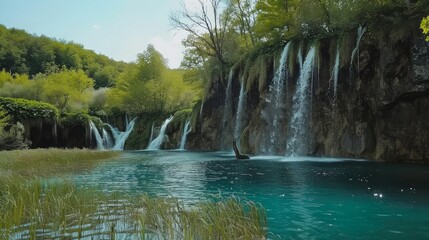 Wall Mural - Majestic waterfall cascading into a serene blue lake surrounded by lush greenery.