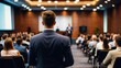 © Ascending Dragon - ビジネス会議で講演する講演者と聴衆の後ろ姿が示すシンポジウムのダイナミズム