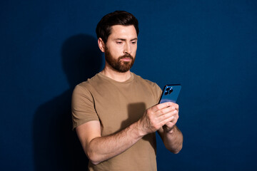 Aufkleber - Photo of young handsome guy brunet hair model in beige t shirt using smartphone texting sms isolated on dark blue color background