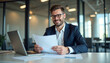 © Ali Hamza Tullah - Smiling businessman working with documents and laptop in modern office