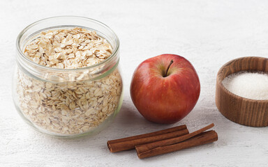 Raw ingredients for oatmeal: rolled oats in a glass jar, cinnamon sticks, apples and sugar