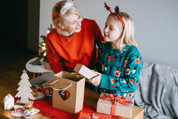 Wall Mural - Mother and daughter exchanging Christmas gifts with joy. Gift exchange, holiday presents, Christmas joy, thoughtful giving, festive surprises.