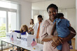 © DragonImages - Portrait of African American woman with baby looking at camera while standing in voting centre