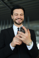 A man in a suit is smiling while looking at his cell phone. He is wearing a tie and he is in a professional setting