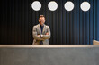 © Moon Safari - Portrait of happy handsome receptionist with arms crossed looking at camera and working at lobby desk