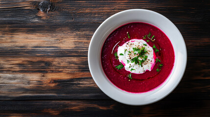 Wall Mural - Beetroot soup being served in a white bowl, seasoned with herbs and cream, on a wooden table