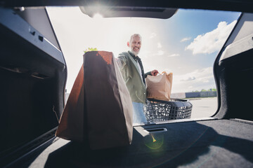 Photo of retired customer male shopping cart loading trunk car paper bags buying food mall parking outside