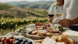 © JoxyAimages - An idyllic setting where a couple enjoys a meal with an assortment of breads and cheeses with glasses of wine, set against rolling hills of a vineyard in daylight.